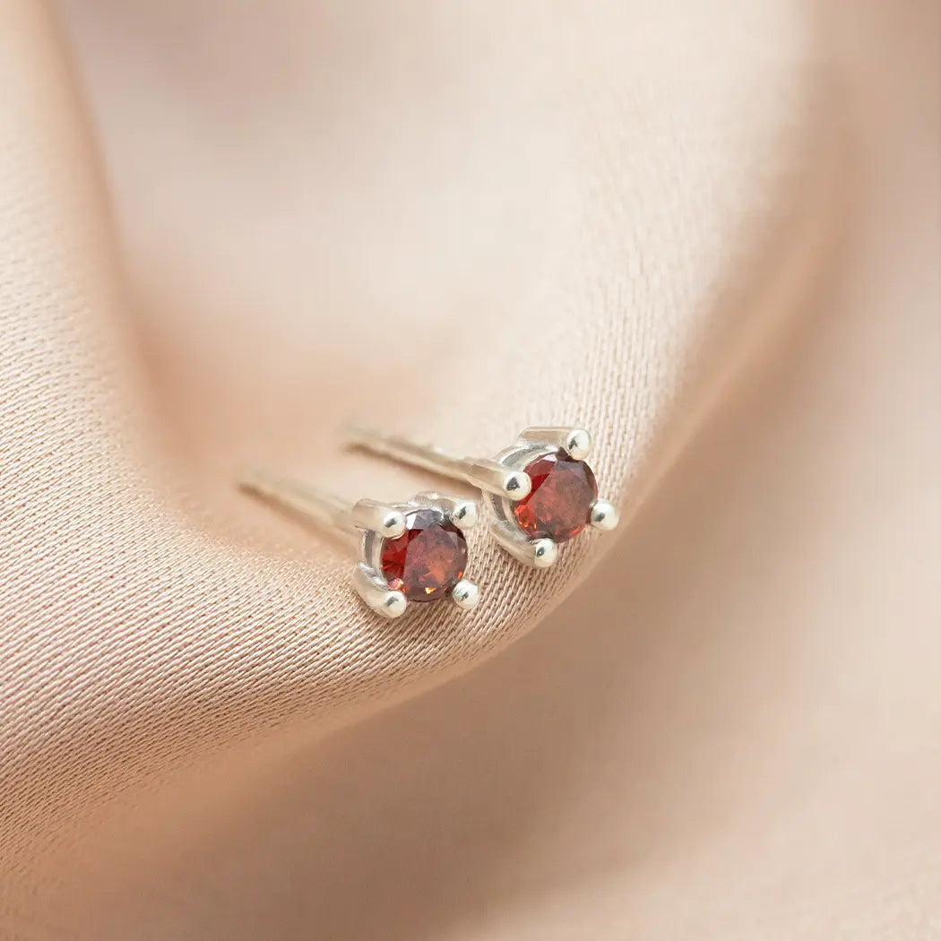 Pair of silver earrings with red gemstones on a beige fabric background