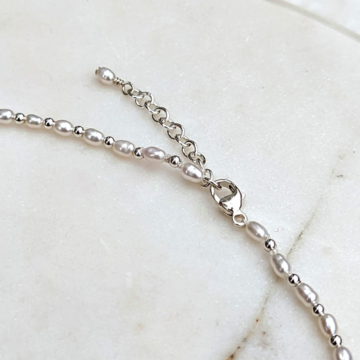 Closeup of silver clasp and chain of tiny pearl and silver bead necklace