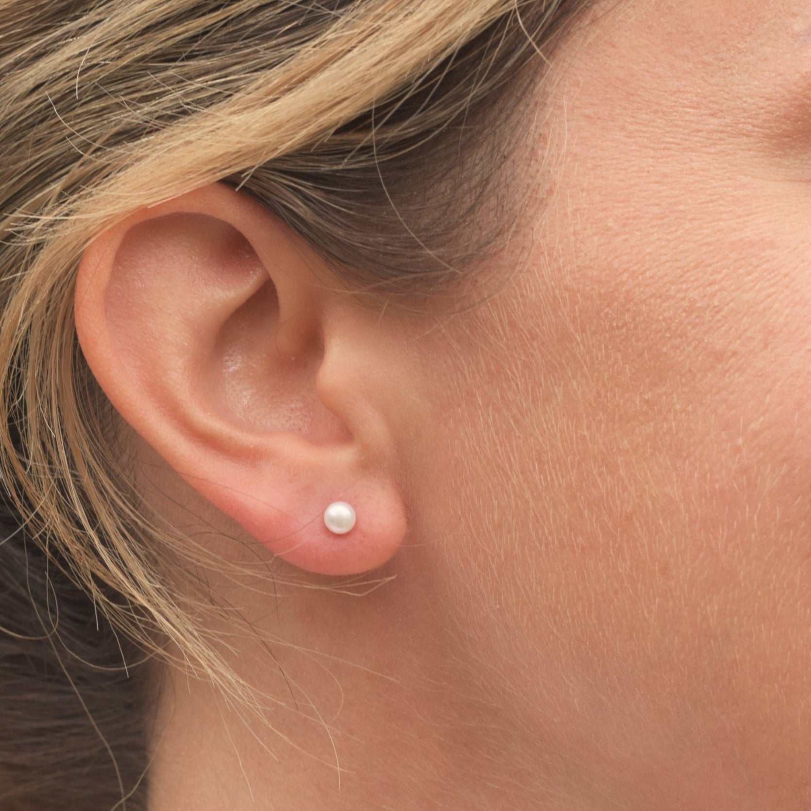 Closeup of model wearing a small white round pearl stud earring